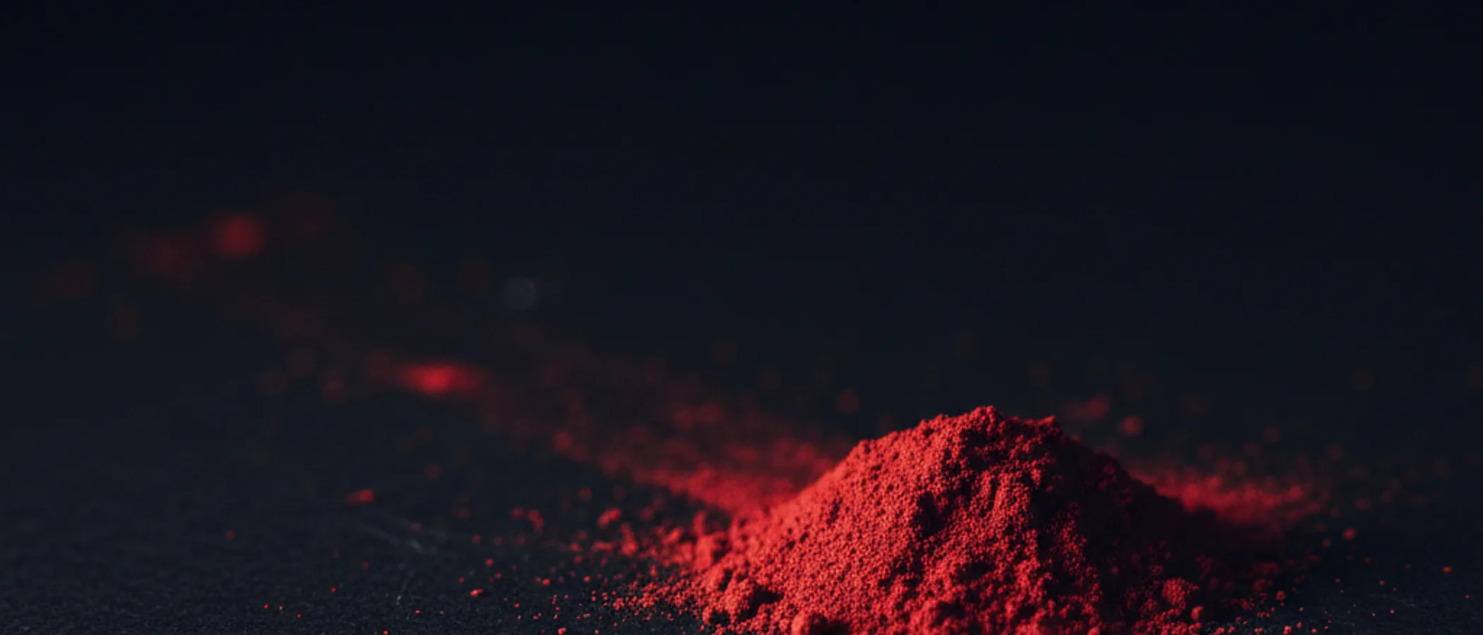 Gundukan pigmen bubuk vermilion di atas permukaan hitam matte, disinari cahaya menyamping.