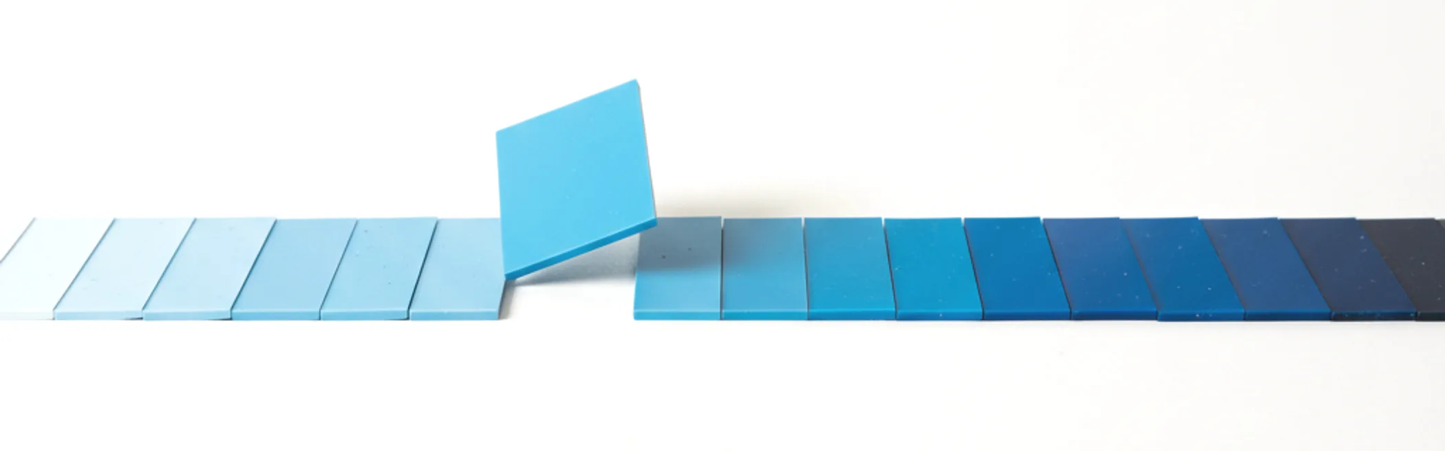 Deretan chip warna plastik tersusun sebagai gradasi biru, dari biru pucat hingga azure pekat, dengan satu chip terangkat dari barisan.